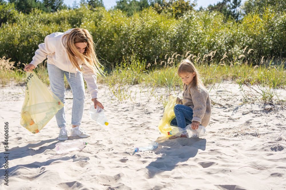 Child and mother volunteers cleaning the sea beach by collecting garbage into plastic bag. Child and mother volunteers cleaning the sea beach by collecting garbage into plastic bag.