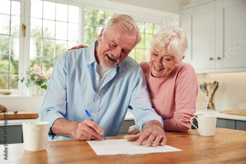 Canvas Print Retired Senior Couple Sitting In Kitchen At Home Signing Financial Document
