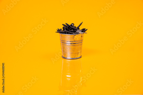 Many metal self-tapping screws made of steel in a glass, in bucket jar. self-tapping screw for metal, for iron, chrome-plated self-tapping screw, on an orange yellow background, photo