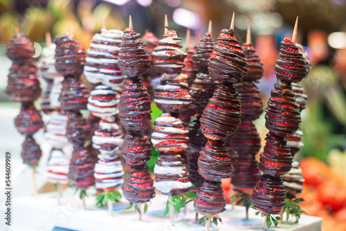 handful of sweet strawberries on a stick  covered in chocolate at a street food shop in a market