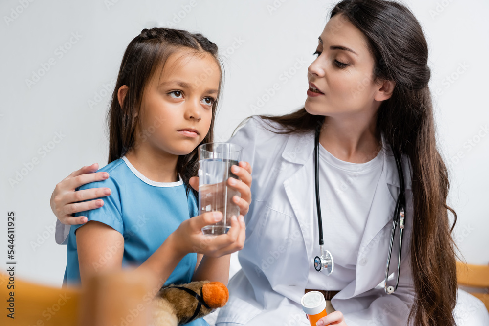 Doctor holding pills and talking to girl with glass of water in hospital ward. Doctor holding pills and talking to girl with glass of water in hospital ward.