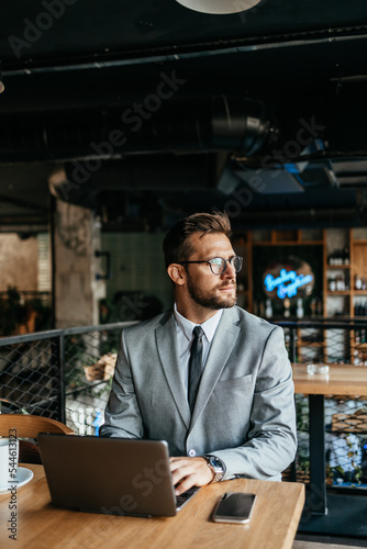 Middle age businessman sitting in cafe bar and enjoying at coffee break between two meetings. He uses laptop computer and he is positive and confident.