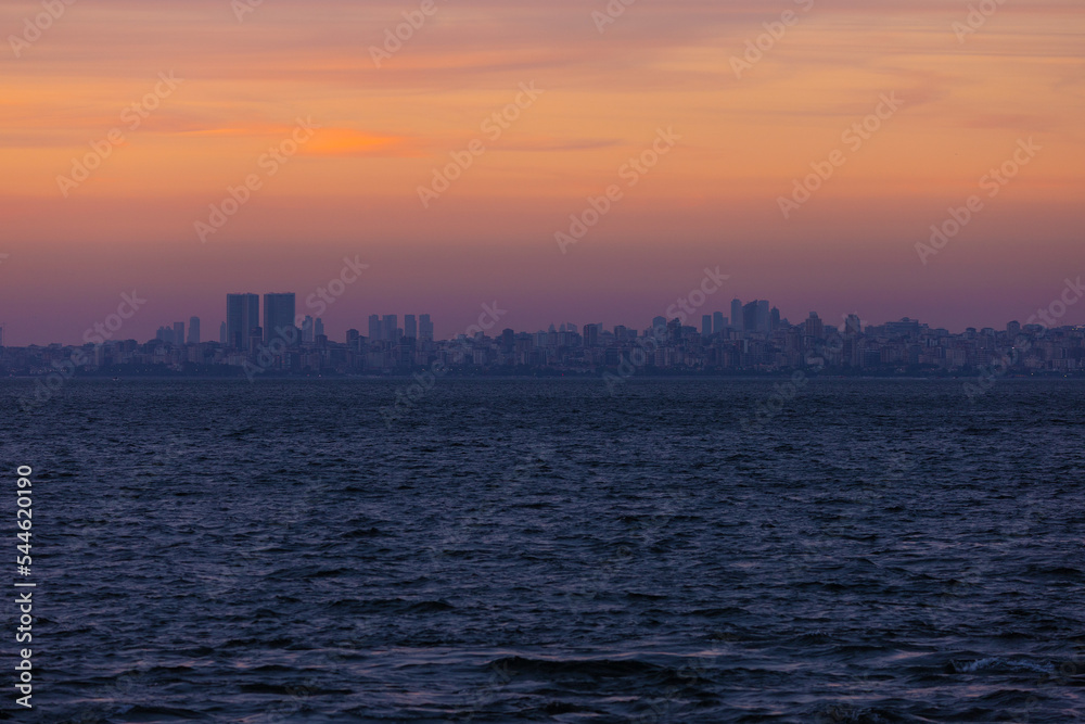 Orange sunset sky and sun over the sea. Silhouette of the city of Istanbul on the horizon.