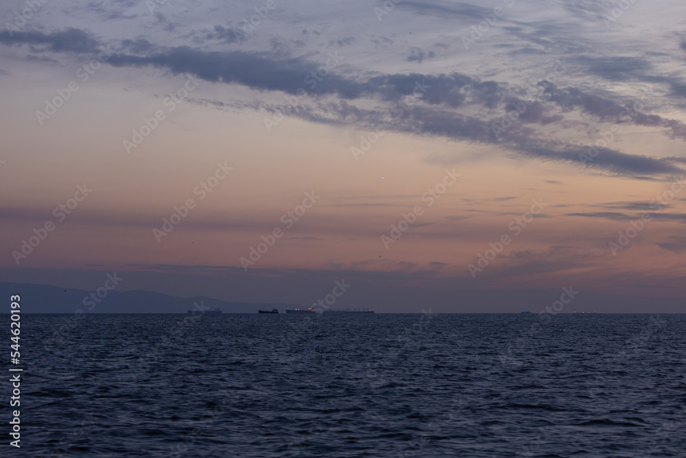 Orange sunset sky and sun over the sea. Water surface and outlines on the horizon.