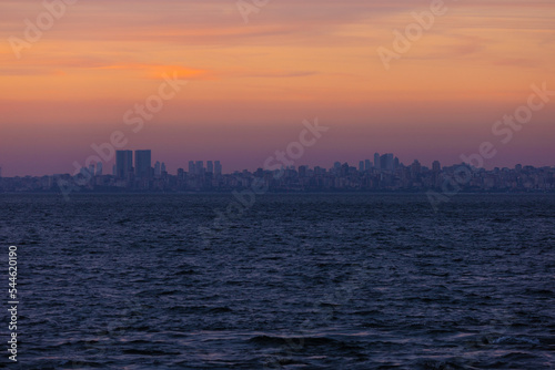 Orange sunset sky and sun over the sea. Silhouette of the city of Istanbul on the horizon.