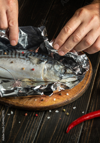 The chef hands preparing mackerel in the kitchen. Wrapping fish in foil before baking in the oven