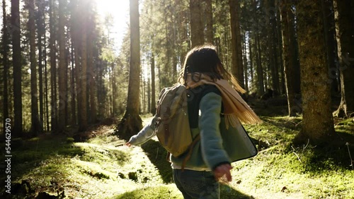 Young woman walking in the forest, wearing fleece and backpack exploring beautiful nature. Having fun, turning around. Slow motion cinematic shot. Sun is shinning in the camera, lens flare.