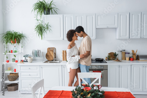 side view of sexy african american couple embracing in modern kitchen with white furniture