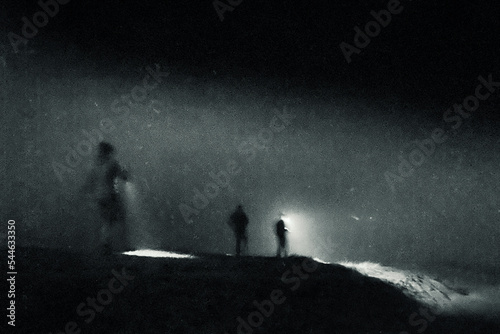 A spooky concept of blurred mysterious figures. Walking on a hill through fog. On an atmospheric foggy winters night.