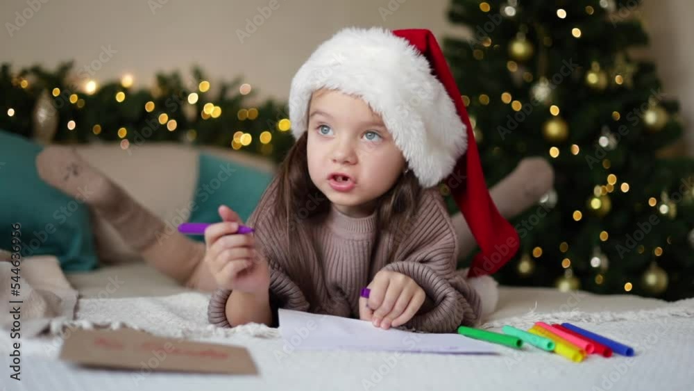 Merry Christmas and Happy Holidays. The little happy girl on the bed wrote a letter to Santa Claus. Decorated bedroom. Lifestyle. Merry Christmas and Happy Holidays. The little happy girl on the bed wrote a letter to Santa Claus. Decorated bedroom. Lifestyle.