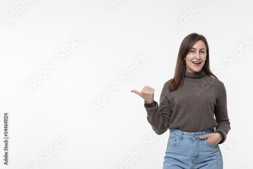 A young positive woman points with her thumb at copy space a white background.An excited, shocked woman shows a place to copy and place an advertisement or advertising text, banner