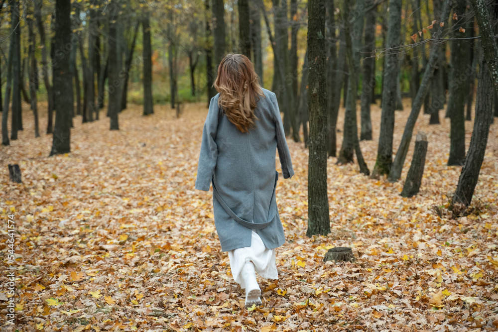girl in a coat in the autumn forest. redhead woman walking in the park. white boots. Close portrait of beautiful woman girl in a coat in the autumn forest. redhead woman walking in the park. white boots. Close portrait of beautiful woman