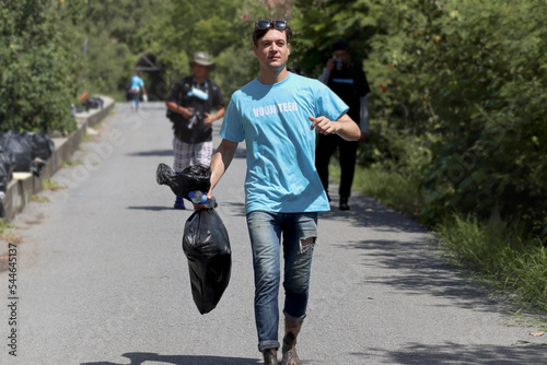 Volunteer in blue t-shirt holding garbage bag while walking down the street to clean, ecology man cleaning and picking up trash to reduce land pollution environmental problem, world environment day.