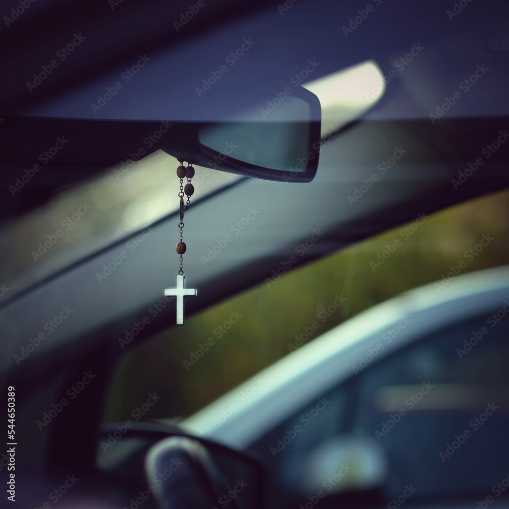 Kette mit christlichem Kreuz hängt als Glücksbringer am Rückspiegel im Auto  Stock-Foto