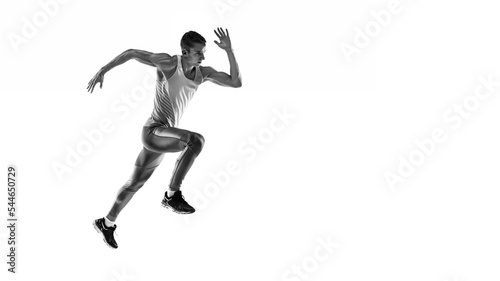 Black and white portrait of muscular male athlete, runner, jogger in motion isolated on white background. Monochrome. Sport, beauty, power and style