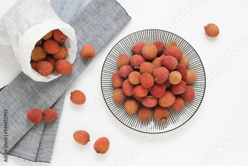 Lychee fruit on Asian plate on white background with whole pieces. Fresh exotic litchi fruits in paper bag. Top view. Photo directly from above.