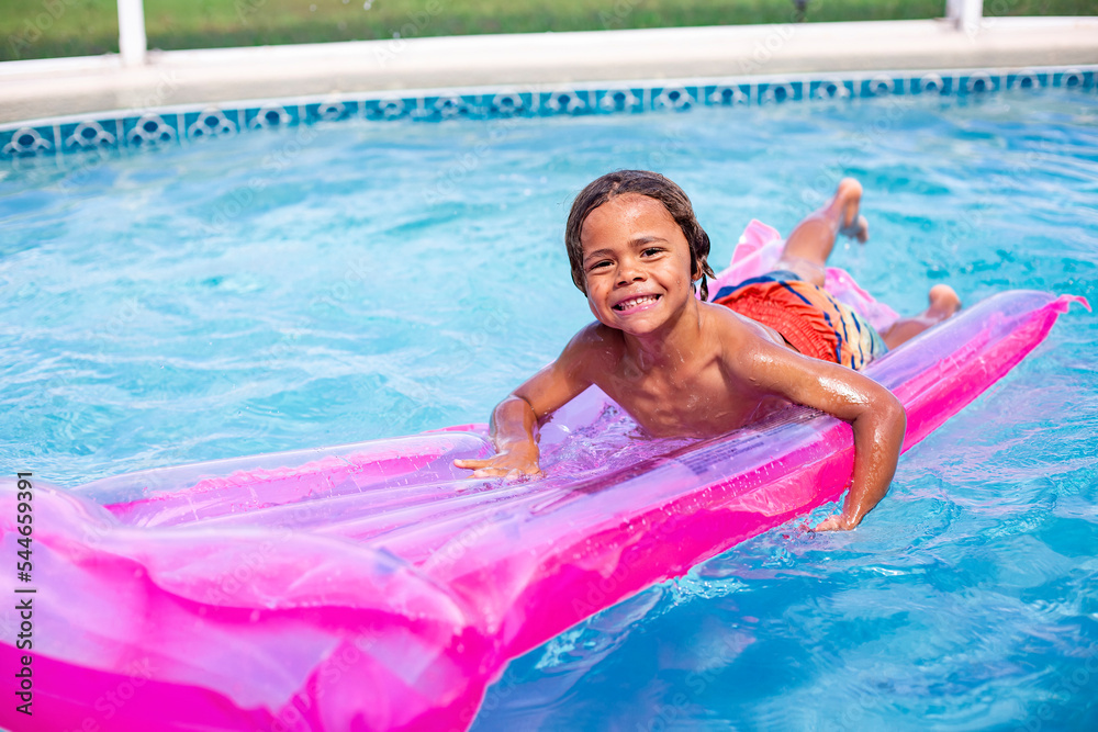 Smiling African American little boy playing in the swimming pool with an inflatable raft. Cute diverse boy having fun in the sun and water 