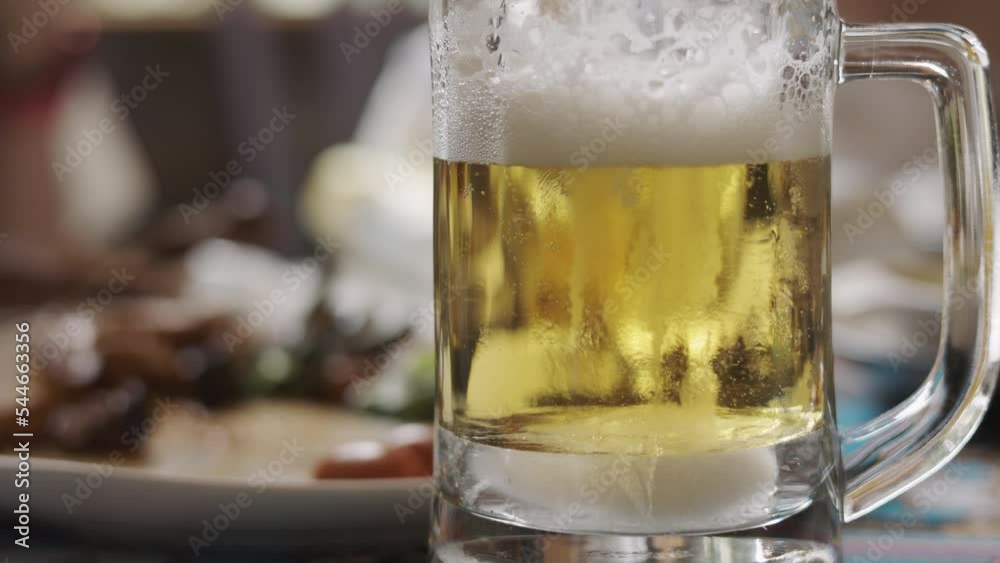 Slow motion 4K with blurred background of frosted glass of beautiful golden and amber beer on the dinner table which looks refreshing and tasty with family or friends dinner or celebratory party. Slow motion 4K with blurred background of frosted glass of beautiful golden and amber beer on the dinner table which looks refreshing and tasty with family or friends dinner or celebratory party.
