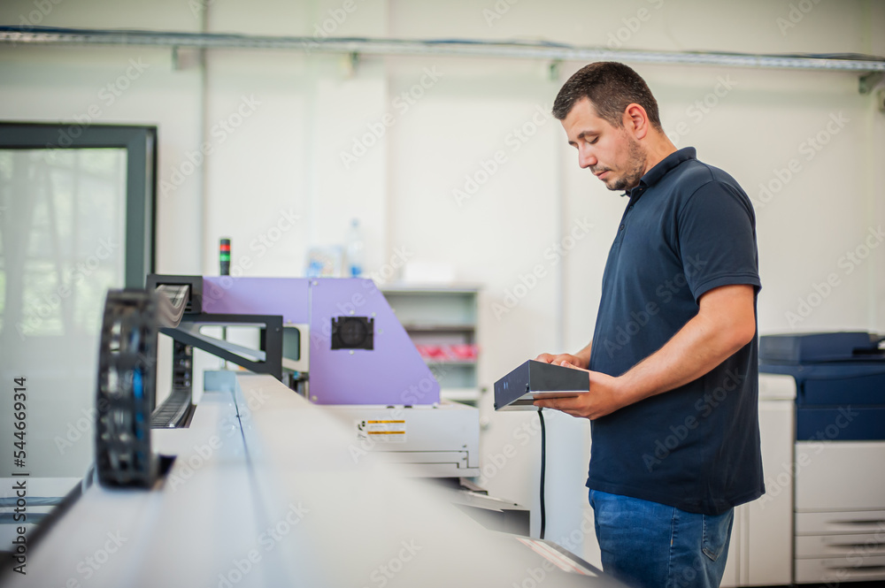 In the printing house, an experienced technician works on a UV printer. Production work. Check the print quality. In the printing house, an experienced technician works on a UV printer. Production work. Check the print quality.