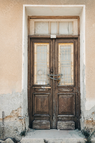 Old shabby wooden front door with metal grates, lock and chain in stucco wall
