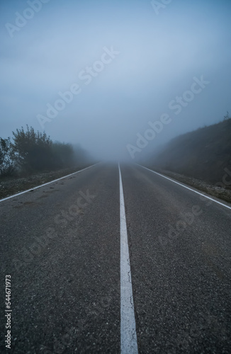 Fotografiet Automobile road in the mountains descending into clouds and fog in late autumn,