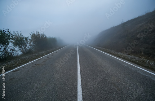 Canvas Print Automobile road in the mountains descending into clouds and fog in late autumn,