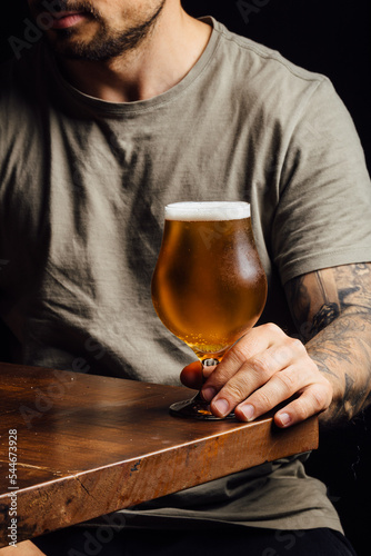 Quadro su tela man holding an India pale ale pint glass on a black background bar