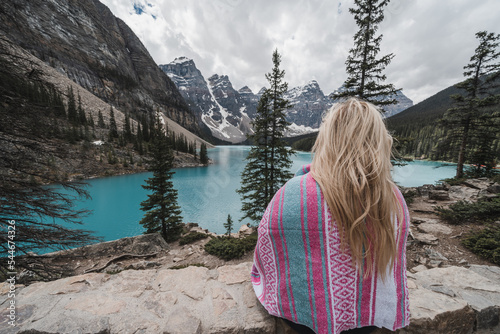 Back view of a blonde woman cuddled in a pink blanket, looking at Moranie Lake in Canada