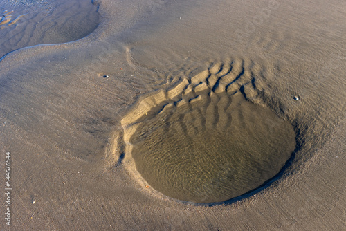 Pfütze mit abstrakt geformter Sandformation im Watt bei Ebbe. photo