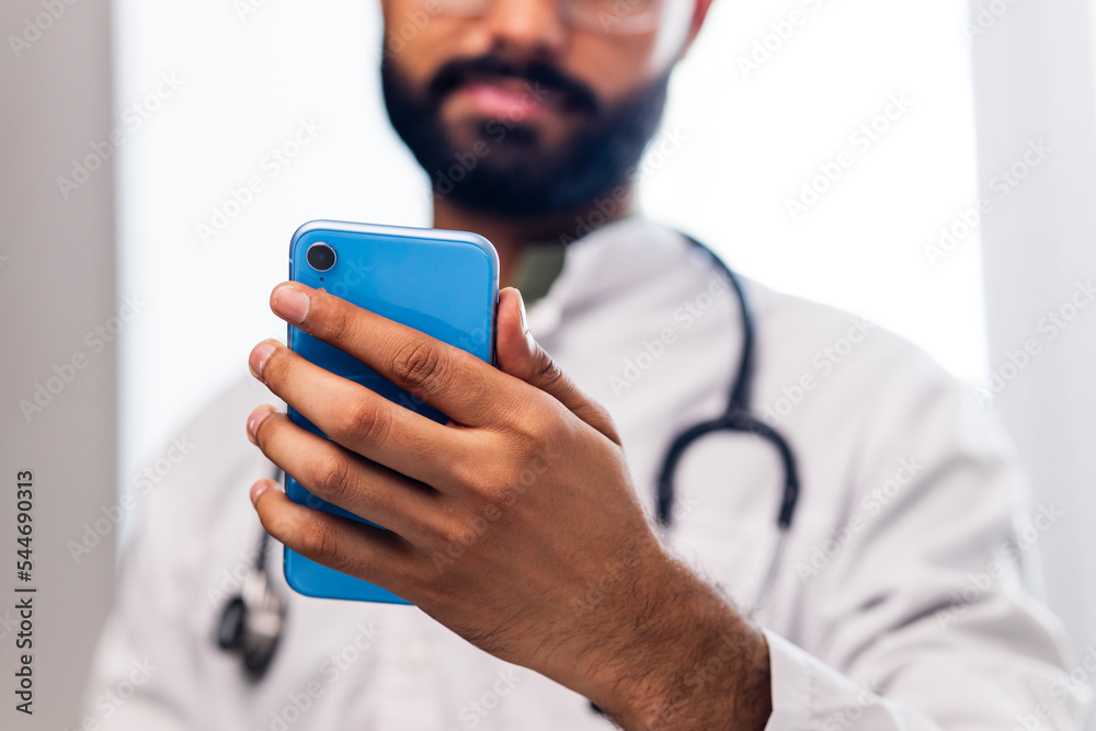 Cheerful indian doctor using application on mobile phone in hospital