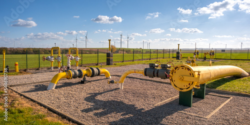 Gas pipes, natural gas transport system. Transmission infrastructure coming from the ground, yellow pipes with valve and flow meter on the background of the wind farm