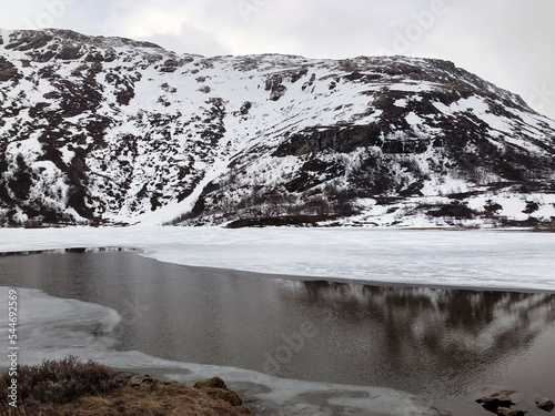 Winter landscape with snowy mountain range and half frozen mountain lake. Norway scenery Scandinavia. White snow covering mountains and lake. Winter scenery. Norwegian nature postcard. Winter season photo