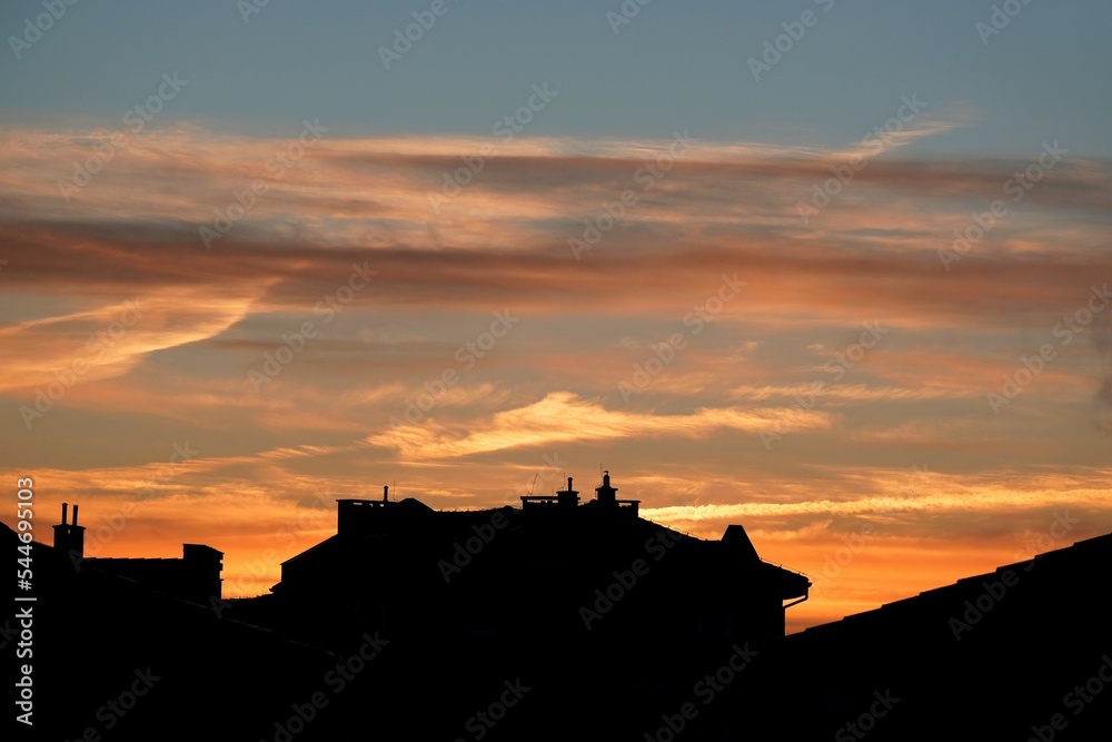 Amazing sunset colours looks like fire on sky over black silhouettes of roofs of city.