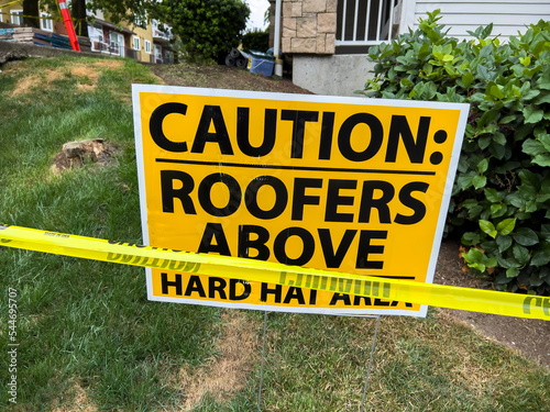 Close up view of a hard hat area sign with caution tape outside of a roof construction zone