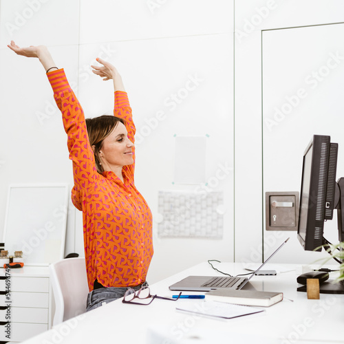 Young smiling business woman sitting in office and doing stretching exercises