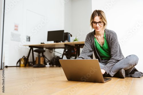 Young business woman sitting on the floor in the office and working with her laptop