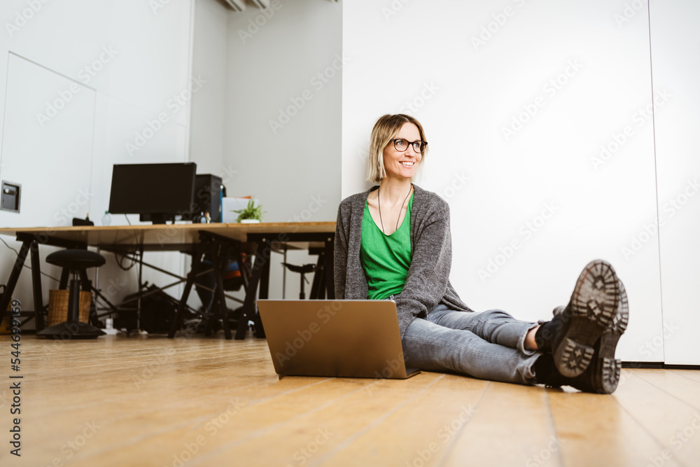 Young relaxed business woman sits with laptop on floor in office and looks up with smile Young relaxed business woman sits with laptop on floor in office and looks up with smile