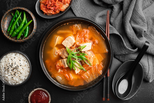 Korean food, kimchi soup with tofu in a ceramic bowl on a black background, top view