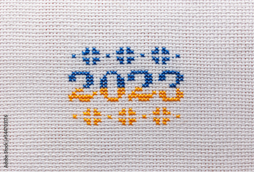 The inscription 2023 is embroidered with yellow and blue threads on a white fabric. photo