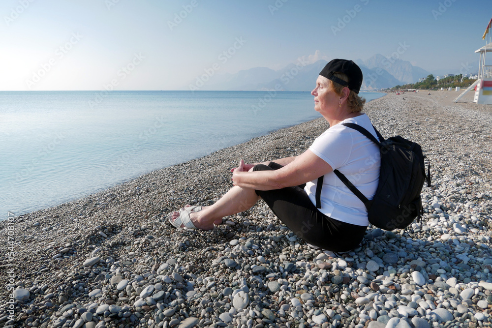 Senior adventurelsageless woman with backpack on the sea beach. Summer active tourism for pensioner. Senior adventurelsageless woman with backpack on the sea beach. Summer active tourism for pensioner.
