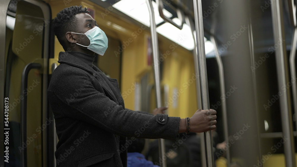 African man adjusting face mask while commuting on train holding bar handrail African man adjusting face mask while commuting on train holding bar handrail