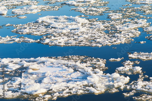 Ice floes float down the river in autumn at sunset. Natural phenomenon before freezing. Reflection of the blue sky in dark water. Natural texture. No people