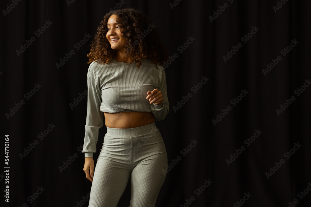A beautiful young african american woman with big curly hair wearing a green dance outfit dancing bachata in a all black room.