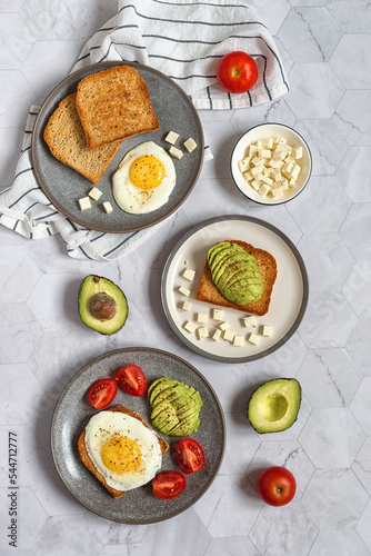 Avocado toast. Healthy breakfast for two: toast bread with fried eggs, avocado, tomatoes and feta cheese on a gray marble table. Healthy food. Healthy lifestyle.
