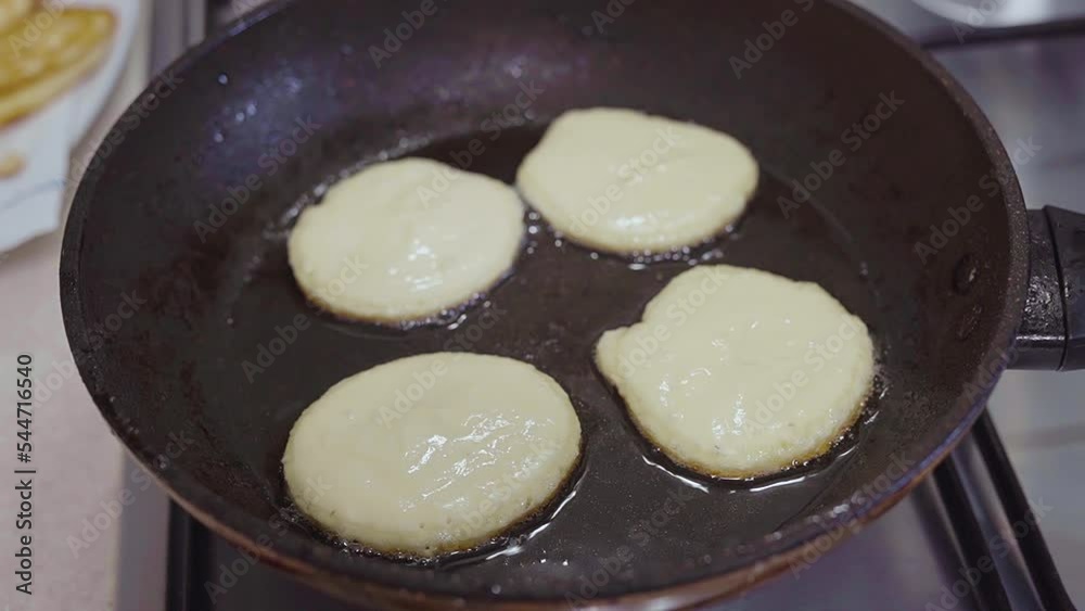 Cooking cheese pancakes in the kitchen. Cheesecakes fried in a black griddle at home Cooking cheese pancakes in the kitchen. Cheesecakes fried in a black griddle at home