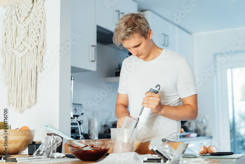 Tableau sur toile Young man cooking brownie cake on the light modern kitchen at home