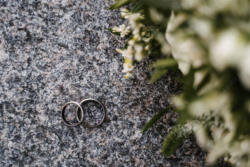 wedding engagement rings made of silver and dark stone lie on a granite surface against the background of the bride's bouquet wedding engagement rings made of silver and dark stone lie on a granite surface against the background of the bride's bouquet
