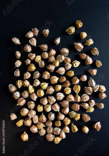 Single layer ground cherries (also known as cape gooseberries) in their yellow, orange and beige papery husks arranged randomly on a black background.  