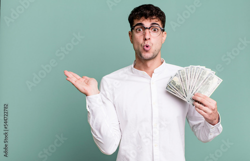 adult man looking surprised and shocked, with jaw dropped holding an object. dollar banknotes concept photo