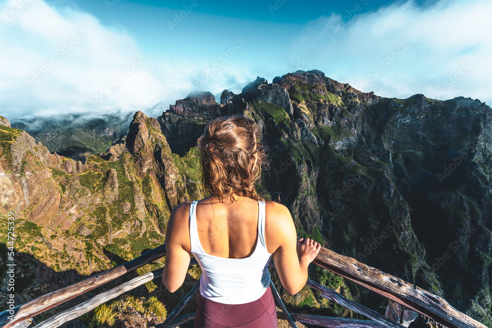 Naklejka premium Woman enjoying the mountain scenery of Pico Ruivo from a viewing platform with very steep cliff in the morning. Pico do Arieiro, Madeira Island, Portugal, Europe.